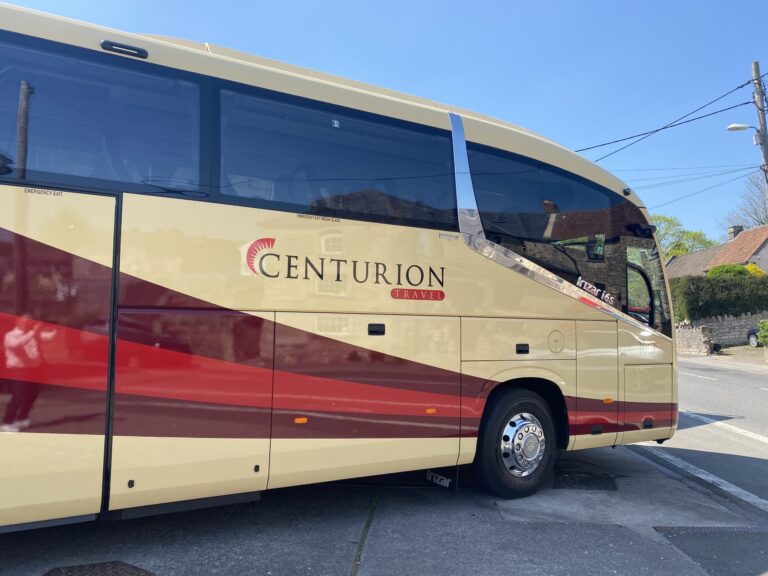 A cream and red Centurion Travel coach parked on a residential street, with clear branding on the side and blue sky overhead.